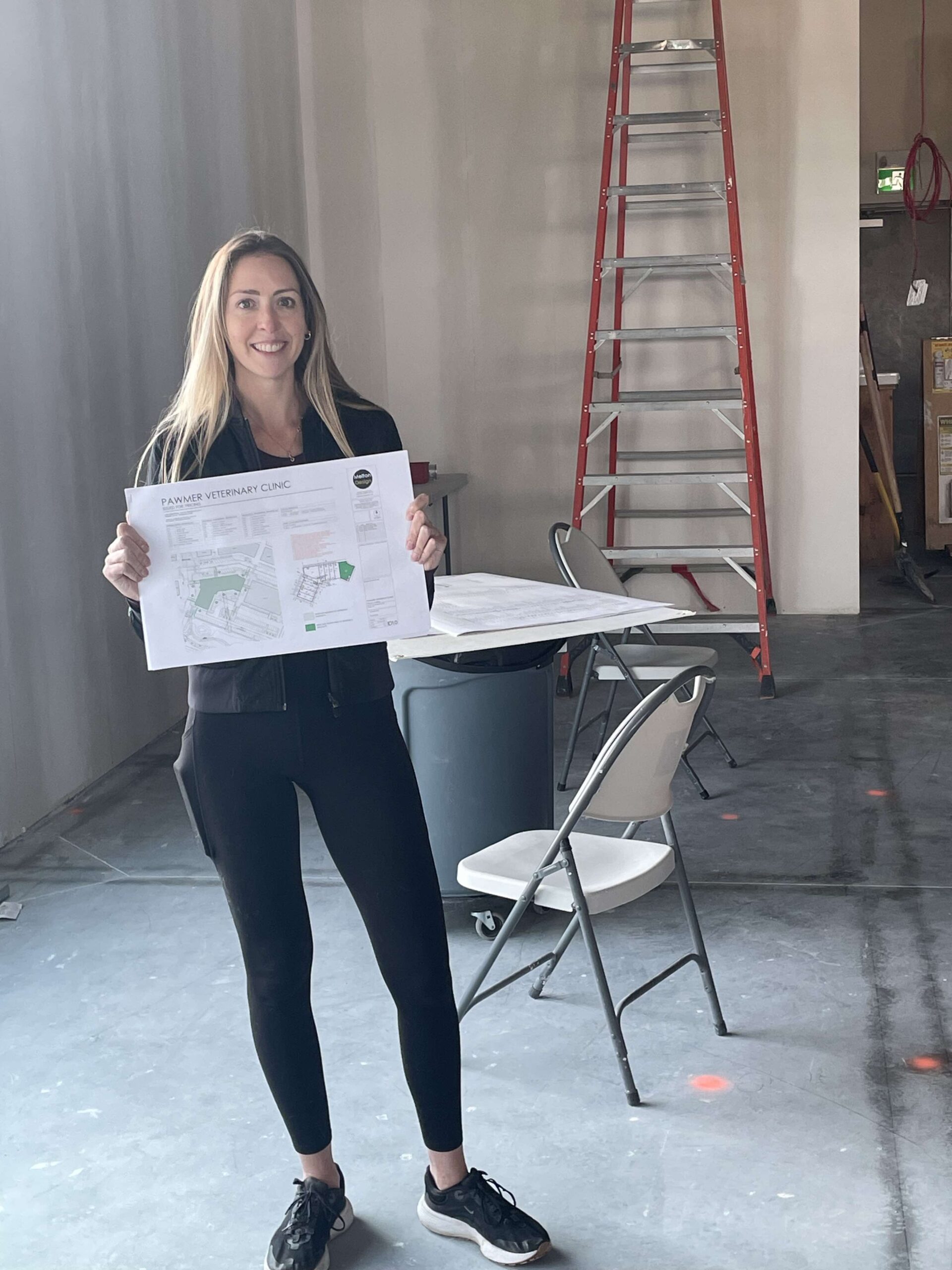 person holding a blueprint with a ladder and chair in the background